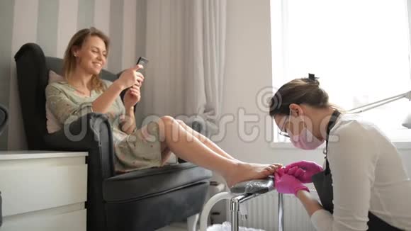 美丽的女人在水疗美容院得到专业的修脚师父正在清理她的指甲客户正在谈视频的预览图