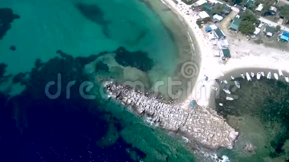海滩的鸟瞰有岩石防波堤和水晶绿松石水旁边是一个小的自然港口在佩岛有渔船视频的预览图