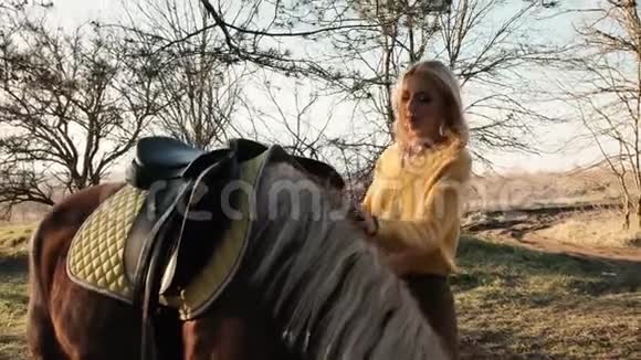 伤心的金发女人正准备骑马把马鞍放在马背上慢动作视频的预览图