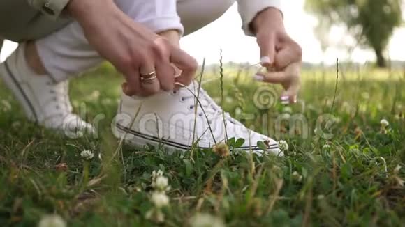 戴着结婚戒指的女跑步者的双手在绿色草地上的白色运动鞋上系紧鞋带视频的预览图