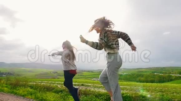 两个笑着的女人在绿色的田野上奔跑跳舞视频的预览图