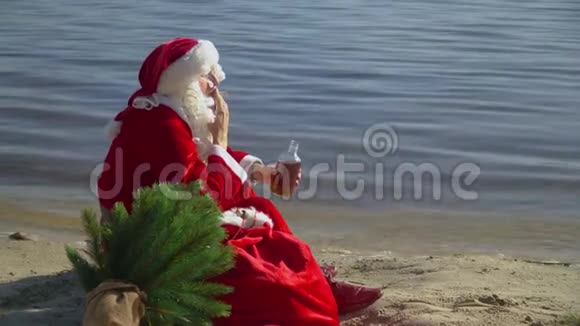 圣诞老人坐在海边的沙滩上拿着一袋礼物抽着烟喝着酒视频的预览图