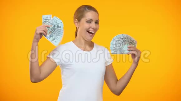 积极的年轻女性手拿着钱跳舞财富兴奋彩票视频的预览图