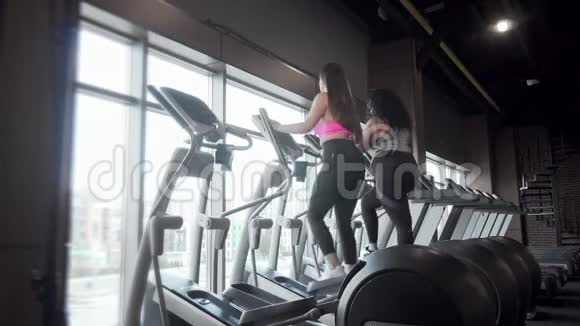 后视图全长镜头两个以上大小的妇女锻炼椭圆教练视频的预览图