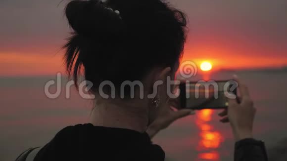 海上日落时分年轻的旅游妇女在电话中拍照的剪影视频的预览图