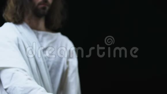 耶稣穿着长袍用木十字架在黑暗的背景下伸出手视频的预览图