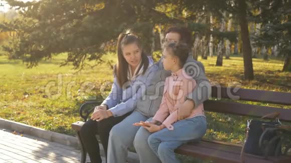 代之间的联系祖母和她的两个孙女坐在公园的长凳上交谈视频的预览图