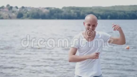 穿着白色T恤在湖边跳舞的秃头肖像视频的预览图