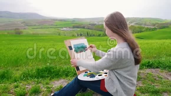 一个身材高大的女人坐在田野上用刷子和栅栏画画视频的预览图