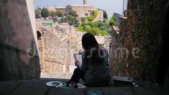 一个年轻的女人坐在楼梯上油漆建筑物背面视频的预览图