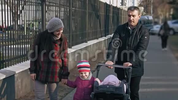 家庭步行在公园步行与婴儿车与一个幼儿和一个34岁的孩子家庭观念户外活动视频的预览图