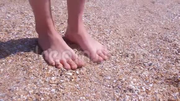 赤脚的女旅行者在海边的贝壳沙滩上按摩脚视频的预览图