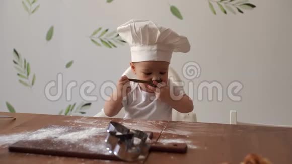 小可爱坐在厨师的帽子里坐在木桌旁品尝面粉视频的预览图