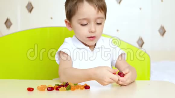幸福孩子的画像一个小男孩坐在桌子旁拿着明亮的水果糖果果酱孩子吃东西视频的预览图
