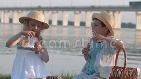 儿童娱乐可爱可爱的戴草帽的男孩和女孩在大自然野餐时吹泡泡视频的预览图
