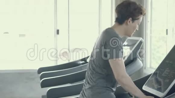 亚洲年轻人在健身房跑步机上跑步锻炼亚洲男人在累的情况下做有氧运动擦汗视频的预览图