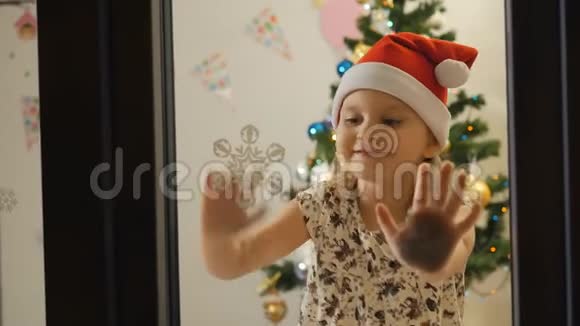 戴着圣诞帽的小女孩晚上坐在窗边的房间里视频的预览图