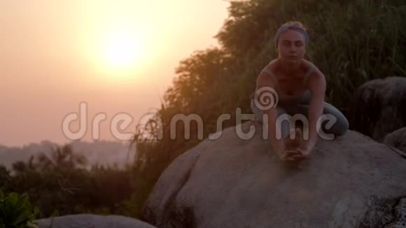 女士在瑜伽体式中放松身体坐在石头上慢动作视频的预览图