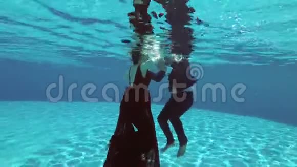 一个穿着红色裙子的漂亮女孩和一个穿西装的男人在游泳池里的水下游泳并为一位摄影师摆姿势视频的预览图