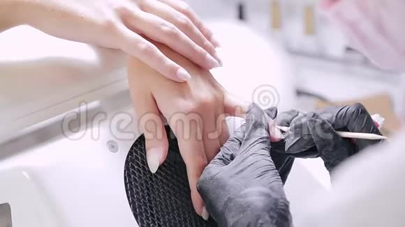 美容店里一位带手套的女美甲师用木棍把顾客指甲上的角质层推开视频的预览图