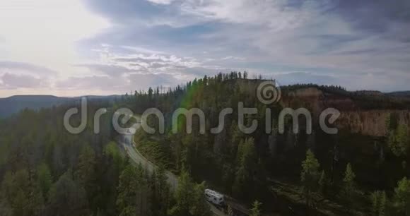 阳光明媚的一天汽车沿着蜿蜒的高速公路行驶在峡谷边缘的绿色松树附近视频的预览图