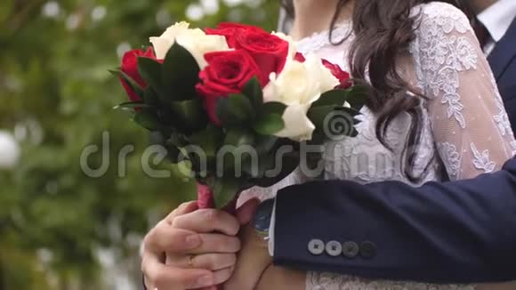 新娘手里捧着五颜六色的玫瑰花穿着白色连衣裙有美丽花朵的女孩拥抱男人的手视频的预览图