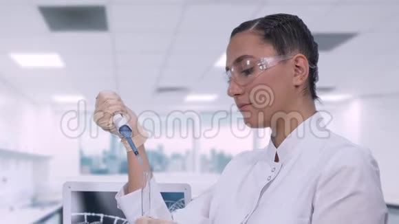 一位女实验室技术人员坐在现代医学实验室笔记本电脑旁的桌子旁检查一个蓝色的样本视频的预览图