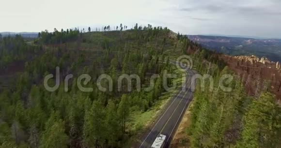 一辆白色大篷车在峡谷悬崖上的森林中沿着公路行驶的空中录像视频的预览图