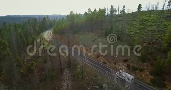 一架白色拖车上的移动摄像机的空中视频它骑在公路上穿过一片绿色的松树林视频的预览图