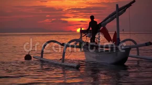 傍晚在平静的海洋港湾中的白色小船美丽的日落景色和当地年轻渔民的渔船视频的预览图