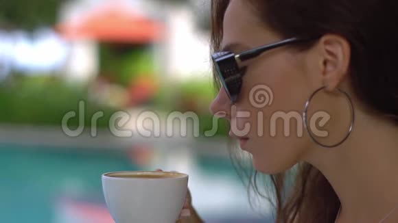 漂亮的年轻女士戴着时尚的太阳镜和大耳环在户外咖啡馆休息喝着卡布奇诺视频的预览图