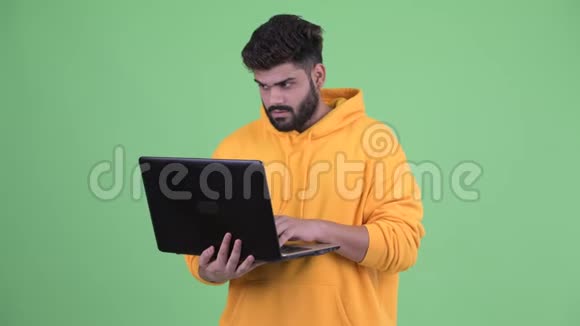 快乐年轻体重超重留着胡子的印度男人在用笔记本电脑思考视频的预览图