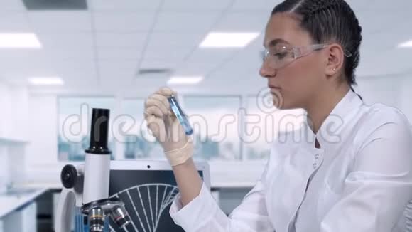 女化验员坐在桌子旁在试管中进行蓝色液体的化验视频的预览图