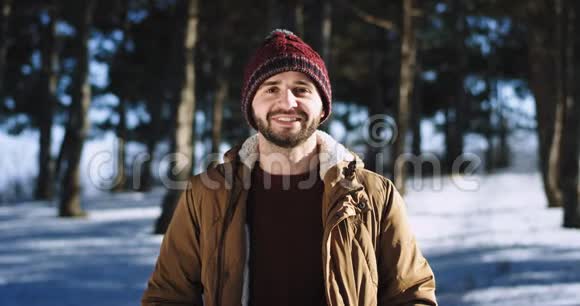 帅哥在镜头前笑得很可爱他在雪林中央戴着帽子视频的预览图