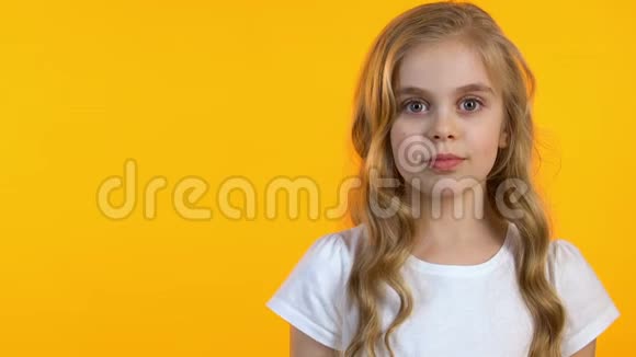 一个漂亮的小女孩在隔离的黄色背景上对着镜头眨眼模板视频的预览图