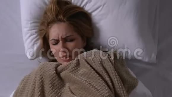 年轻的患病妇女冻得瑟瑟发抖床上盖着毯子有流感症状视频的预览图