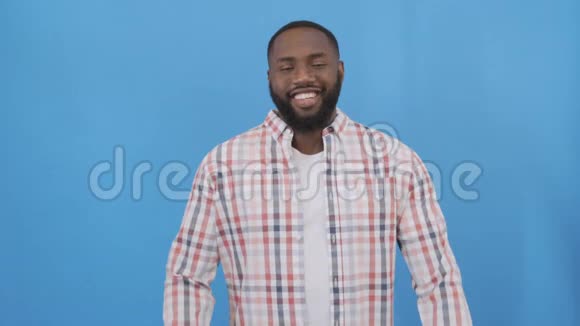 穿格子衬衫的美国黑人帅哥蓝色背景上快乐的微笑男人4K视频的预览图