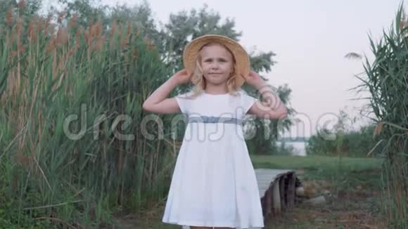 大自然中蓝眼睛戴着草帽穿着白色连衣裙的小可爱女孩的画像视频的预览图