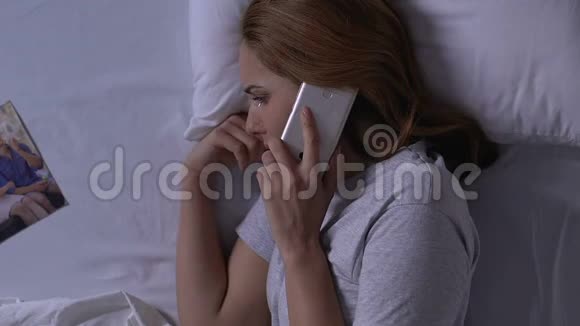 在床上哭的女人看着全家福打电话给前夫亲戚视频的预览图
