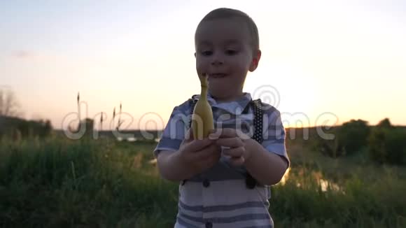 欢乐的男孩在日落时分带着香蕉在夏天的田野上缓慢地奔跑视频的预览图