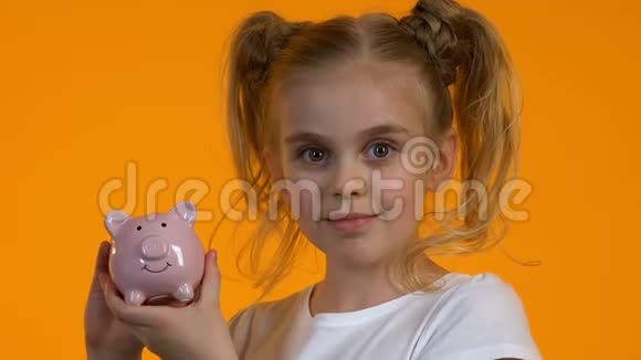 可爱的小女孩拿着硬币和微笑的储蓄罐视频的预览图
