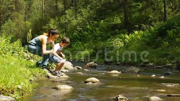 美丽的母亲和她的儿子在山溪玩纸船视频的预览图