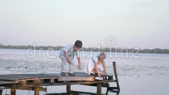 户外娱乐活动木桥上可爱的小男孩小女孩正在水上放着纸船视频的预览图