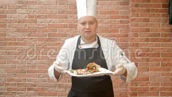 身着制服的友好厨师向我们展示了一盘海鲜沙拉并与摄像机交谈视频的预览图