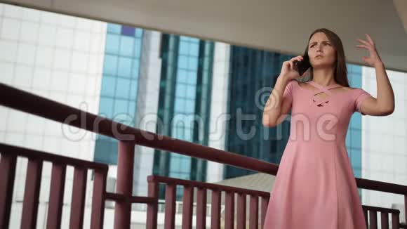 女孩拿着智能手机穿着粉红色的裙子有感情地说话挥舞着她的手视频的预览图