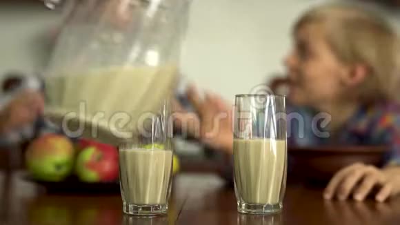 妈妈的手在杯子里倒牛奶为前景中的孩子们男孩和女孩在喝牛奶视频的预览图