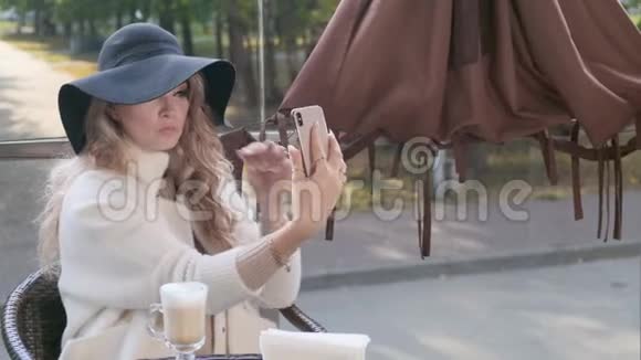 一位美丽的女士在户外咖啡馆里摆着智能手机自拍视频的预览图