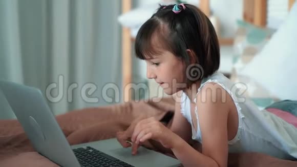 小女孩躺在床上用笔记本电脑玩电脑游戏慢动作视频的预览图