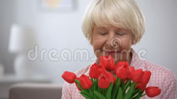 可爱的老年女性嗅着郁金香在镜头前微笑视频的预览图