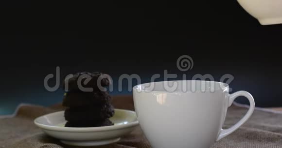 将热巧克力倒入棕色桌布上的白色陶瓷杯和模糊的dakr巧克力蛋糕上为每个人提供美味的饮料视频的预览图